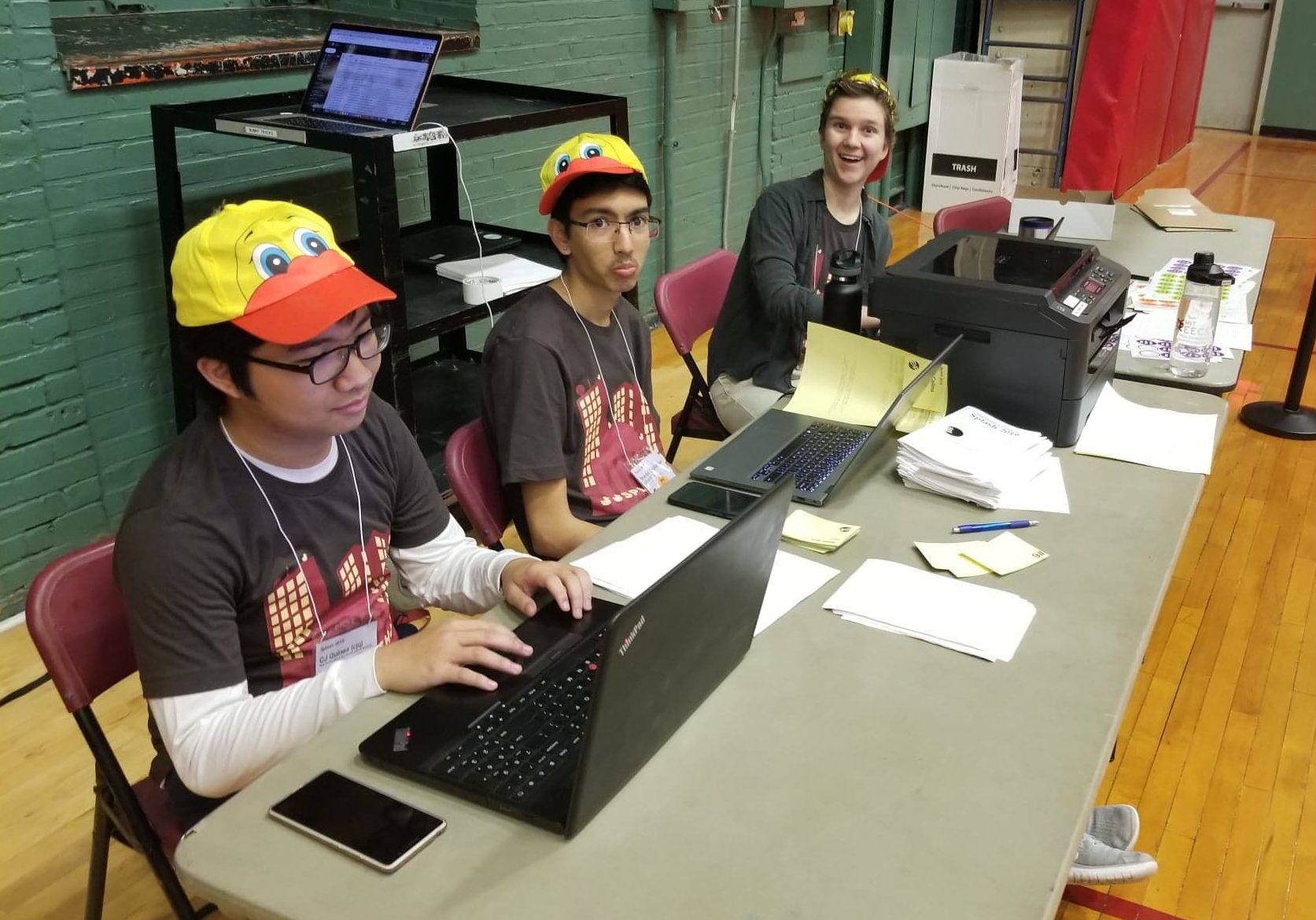 three people on a table. i am leftmost, on my laptop. two other people are looking at the camera.