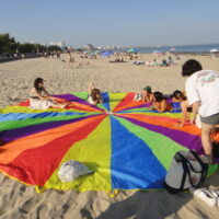 people on the beach sitting on a rainbow parachute